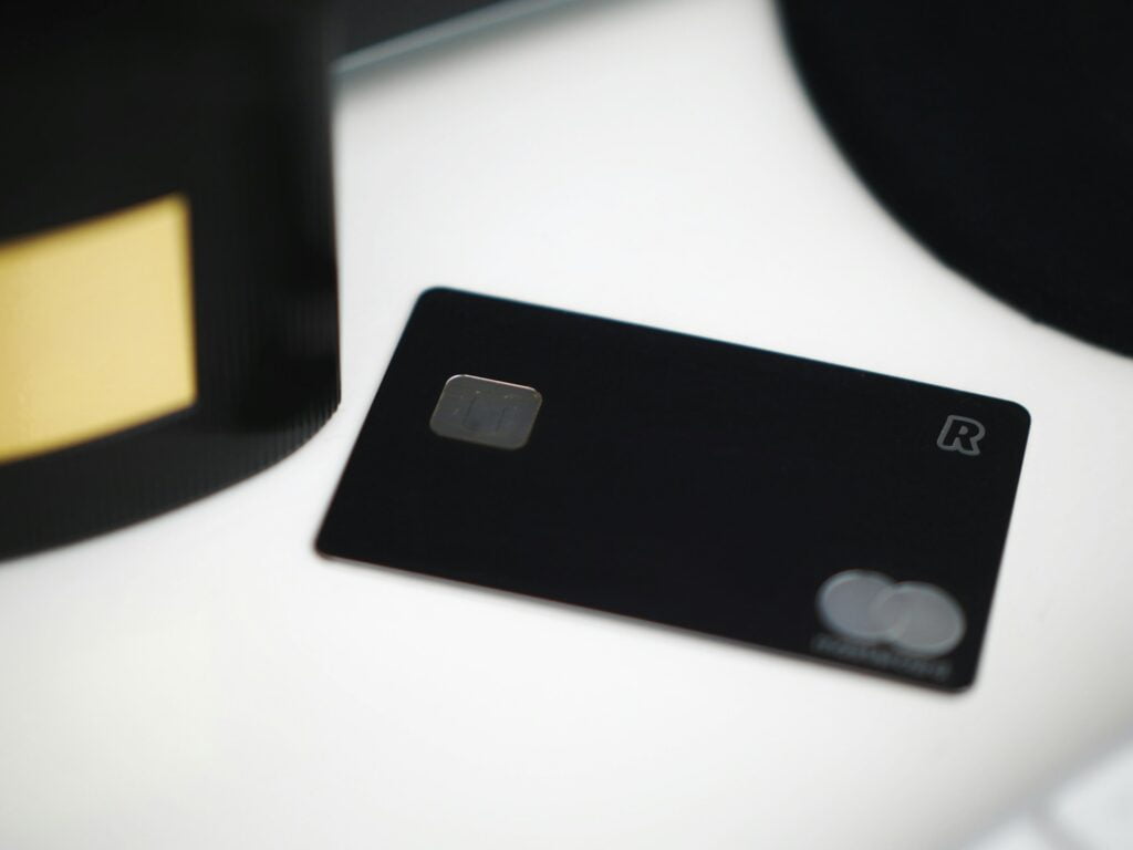 Um cartão de crédito preto com o símbolo da Mastercard desfocado em cima de uma mesa branca.