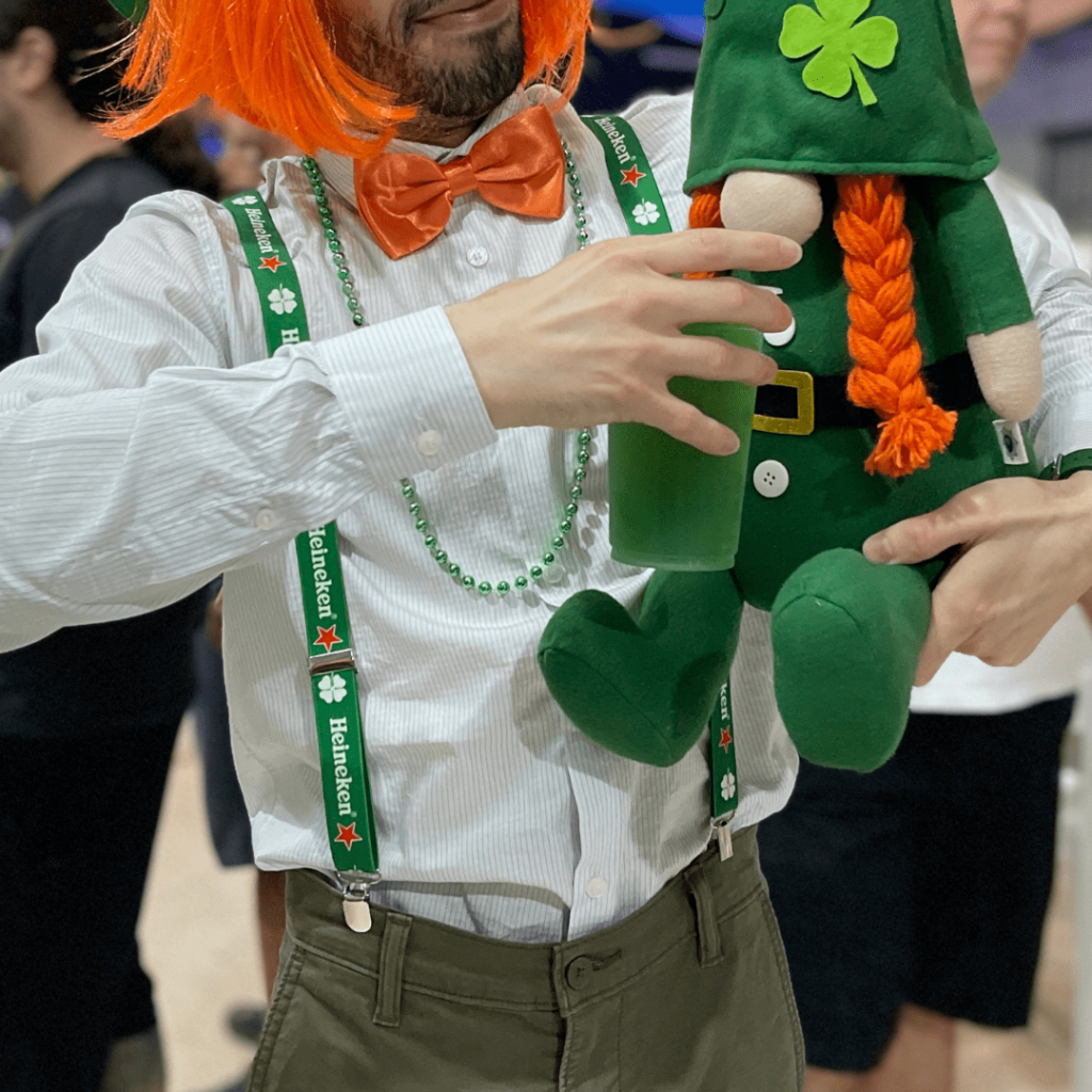 Pessoa fantasiada de Leprechaun com um chopp verde e um boneco do Leprechaun para o Saint Patrick's Day.